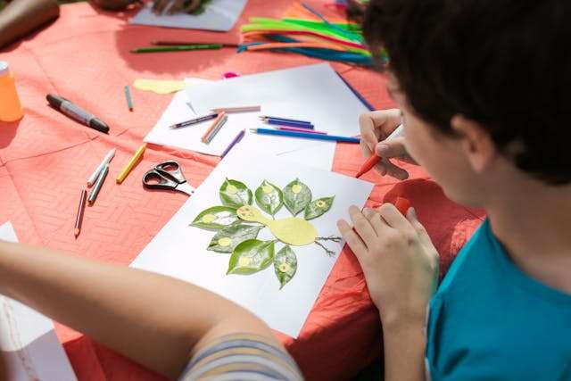 A child creating leaf art with colored pencils and craft supplies, symbolizing creativity and curiosity as signs of intelligence.