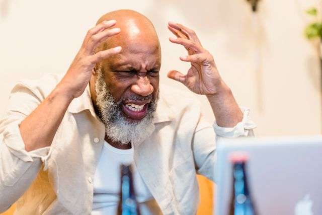 Frustrated senior man holding his head in anger while looking at a laptop screen, illustrating a moment of intense stress from the How to Control Anger Anytime guide.