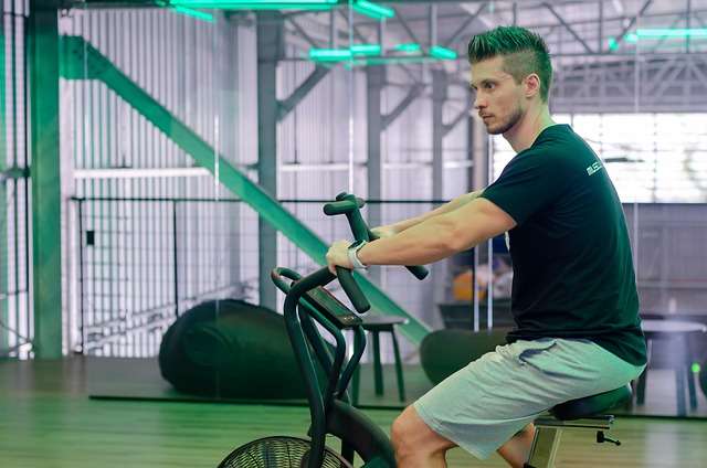 A man intensely working out on a stationary exercise bike in a gym, highlighting physical exercise as a healthy strategy for how to control anger anytime.