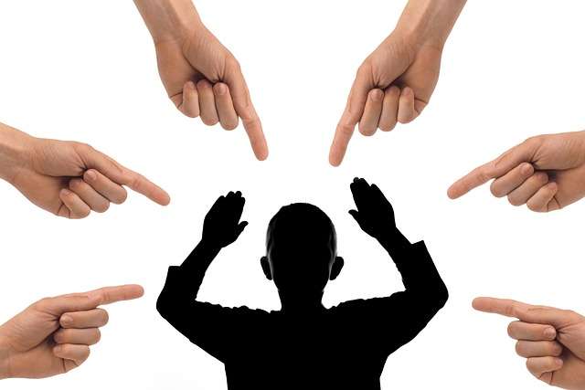Black silhouette of a person with hands raised in defense surrounded by multiple hands pointing at them, illustrating the pressure of social anxiety and how to stop caring what people think.