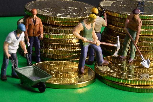 Miniature figurine workers laboring on stacks of gold coins, representing hard work and wealth building inspired by The Richest Man In Babylon.