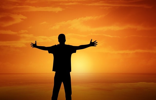Silhouette of a person standing on the beach with open arms during a warm sunset, representing simple ways to find joy and happiness in everyday life.